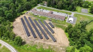 An aerial view of a building complex with parking areas and adjacent solar panel installations surrounded by greenery and trees.